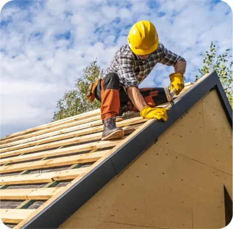 Roofer in a yellow hard hat nailing along an open roof deck