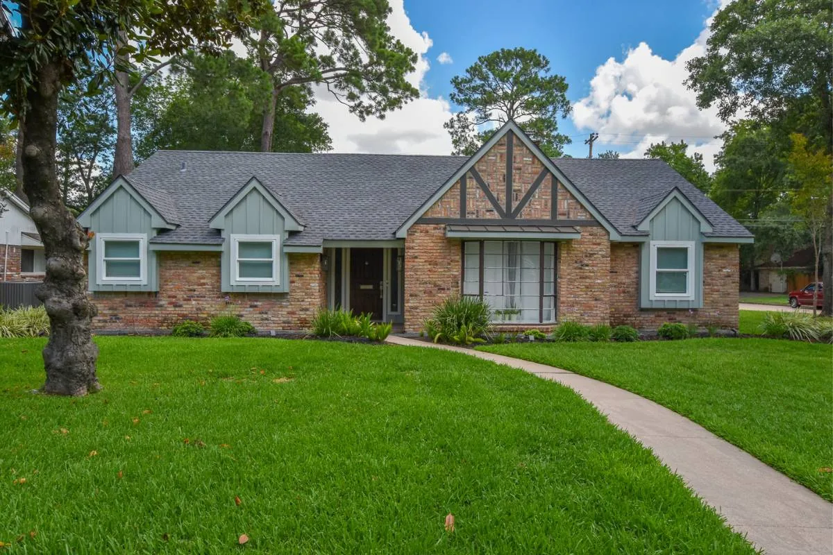 Brick and sage-green cottage with a gray shingle roof